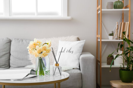 Vase with beautiful daffodils and reed diffuser on table in roomの写真素材