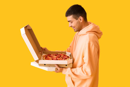 Handsome young man holding boxes with fresh pizza on yellow backgroundの写真素材