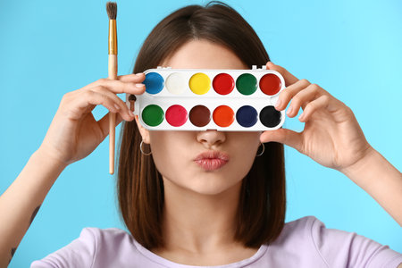 Young female artist with paints and brushes on color backgroundの写真素材