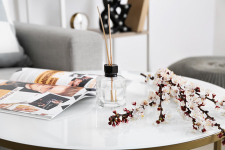 Blooming spring branches, reed diffuser and magazine on table in roomの写真素材