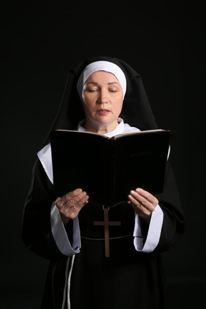 Mature nun reading Holy Bible on dark backgroundの写真素材