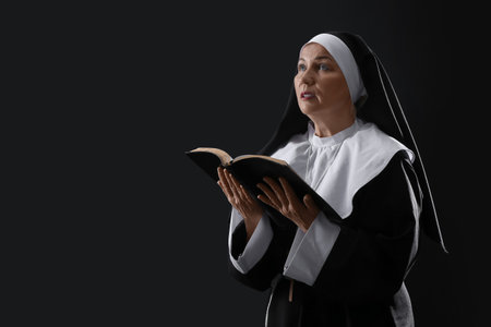 Mature nun reading Holy Bible on dark backgroundの写真素材