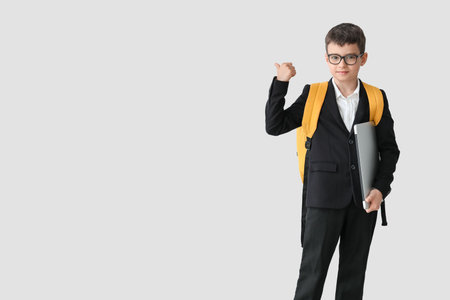 Little schoolboy with laptop pointing at something on light backgroundの写真素材