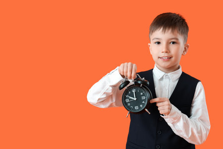 Little schoolboy with alarm clock on color background