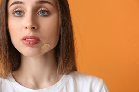 Young woman with plaster onto her face on color background, closeupの写真素材