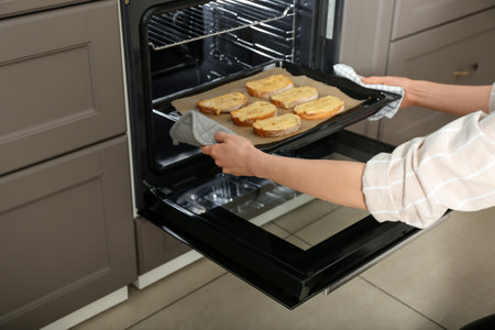 Woman taking baking sheet with toasted bread out of oven, closeup