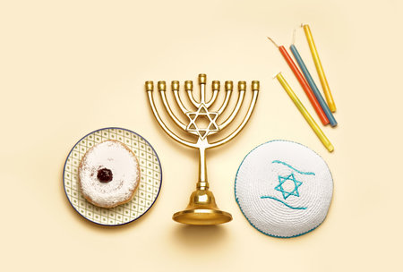 Menorah with donut, Jewish hat and candles for Hannukah celebration on beige background