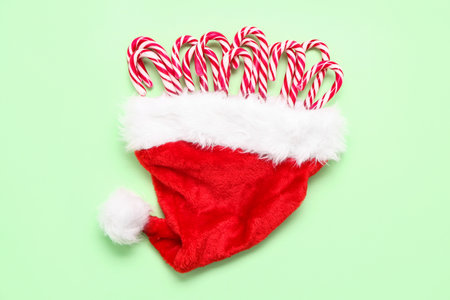 Santa hat with sweet candy canes on color background