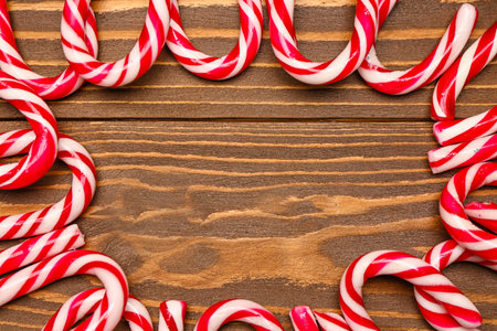 Frame made of tasty candy canes on wooden background, closeup