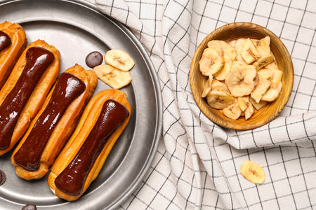 Plate of tasty chocolate eclairs and banana on fabric background, closeup