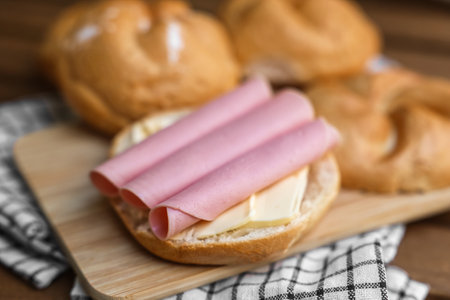 Delicious kaiser rolls with butter and ham on wooden boardの写真素材