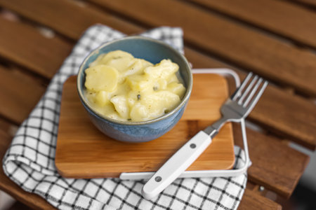Bowl with creamy potato salad, fork and napkin on wooden tableの写真素材