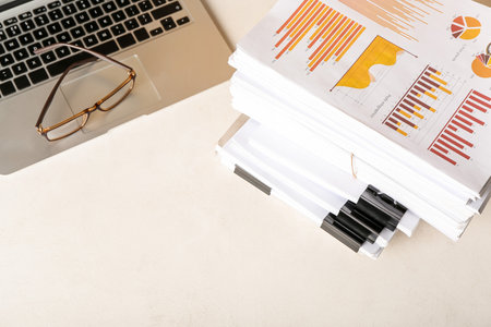 Stack of documents with diagrams and laptop on light table