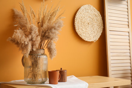 Stylish vase with cup on table near color wall