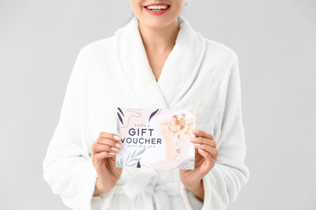 Young woman with gift certificate for massage on light backgroundの写真素材