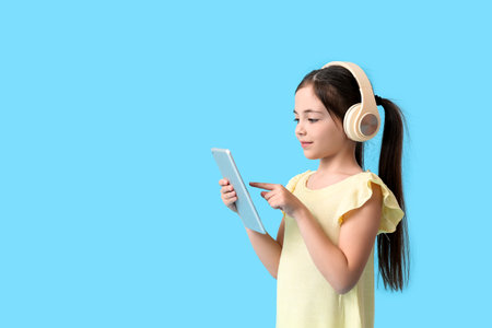 Little girl with tablet computer and headphones on color background
