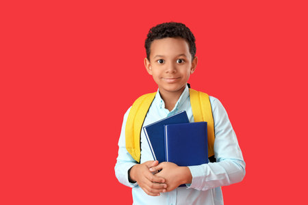 Little African-American schoolboy with books on color background