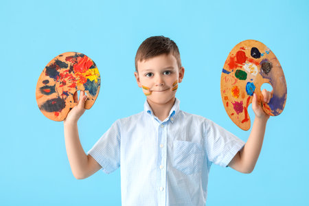 Cute little boy with palette paints on color backgroundの写真素材