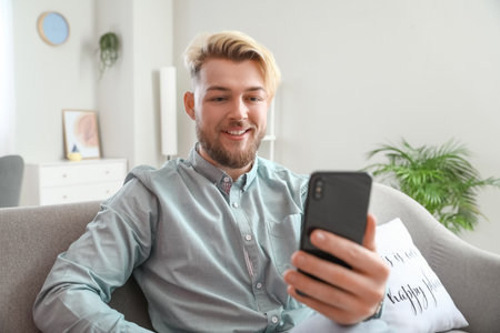 Young man with mobile phone video chatting at homeの写真素材