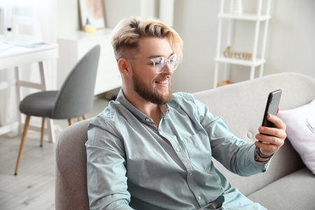 Young man with mobile phone video chatting at homeの写真素材