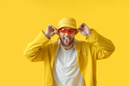 Handsome young man showing tongue on color background