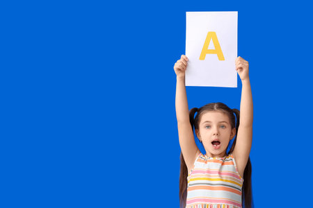Little girl holding paper sheet with letter A on color backgroundの写真素材