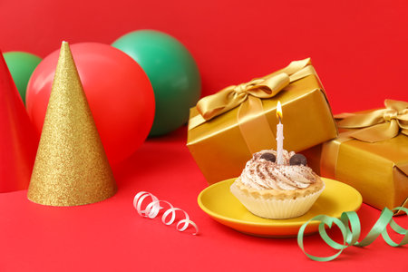 Birthday cake, party hat, gifts and balloons on red backgroundの写真素材
