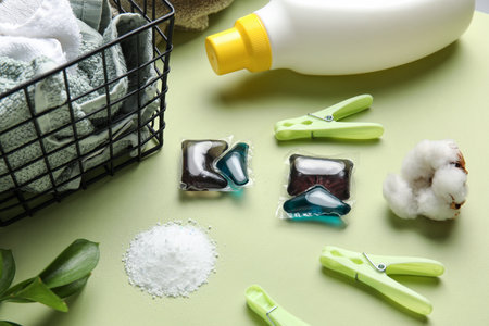 Laundry detergents, towels, basket and clothes pins on green background