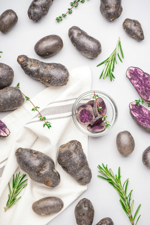Composition with cut and whole purple potatoes and herbs on white backgroundの写真素材