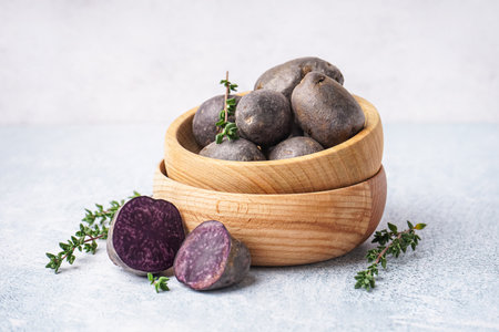 Wooden bowls of raw purple potatoes and thyme on light backgroundの写真素材
