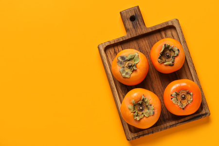 Wooden board with fresh ripe persimmons on color backgroundの写真素材
