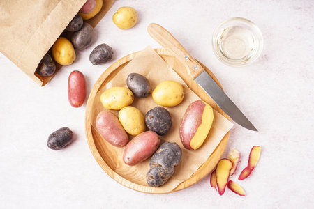 Wooden plate with different raw potatoes and knife on light backgroundの写真素材