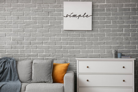 Comfortable sofa and chest of drawers near gray brick wallの写真素材