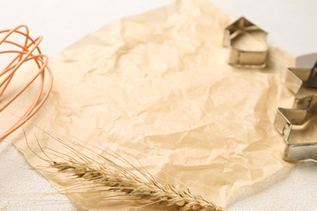 Baking paper, whisk, wheat ear and cookie cutters on light background, closeupの写真素材
