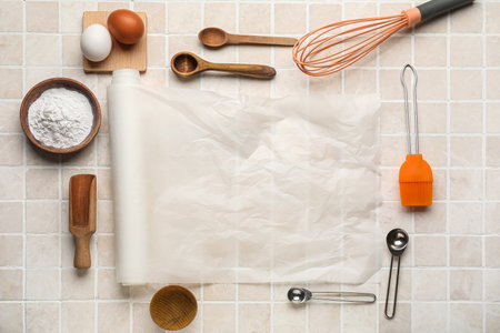 Baking paper with kitchen supplies, flour and eggs on beige tile backgroundの写真素材