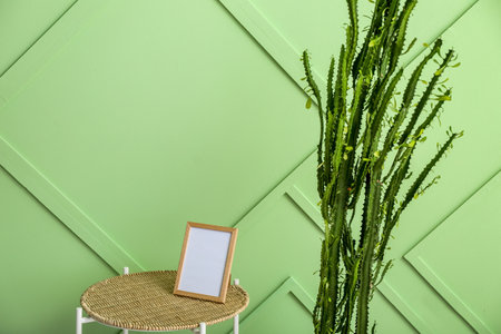 Table with blank photo frame and cactus near green wall