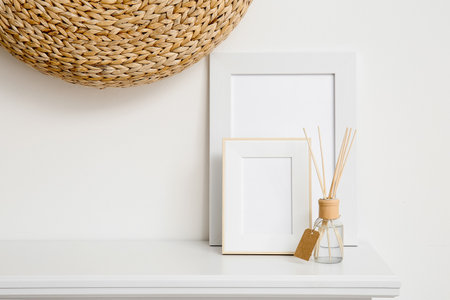 Blank photo frames and reed diffuser on shelf near white wallの写真素材
