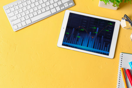 Tablet computer with stock data and keyboard on yellow background. finance trading