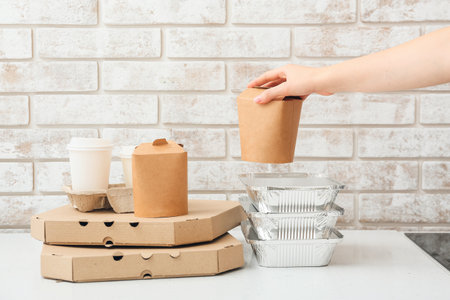 Female hand with box and set of food delivery containers on white table near light brick wallの写真素材