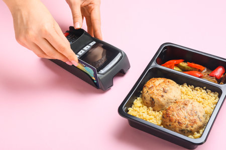 Woman using bank terminal to pay for food delivery on color background, closeup