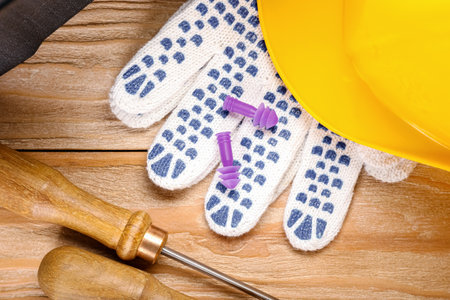 Earplugs, gloves, hardhat and screwdrivers on wooden background