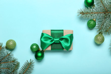 Beautiful gift box tied with green ribbon, fir branches and Christmas balls on color backgroundの写真素材