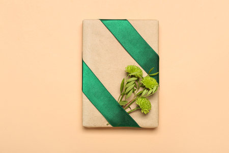 Gift box tied with green ribbon and chrysanthemums on color backgroundの写真素材