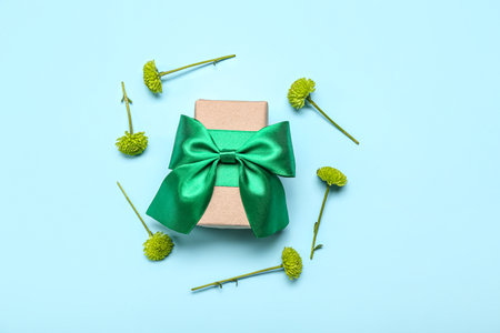 Beautiful gift box with green bow and chrysanthemum flowers on color backgroundの写真素材
