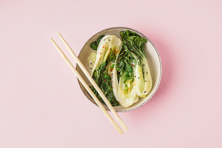 Bowl of tasty stewed pak choi cabbage and chopsticks on pink backgroundの写真素材