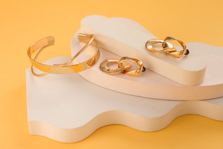 Decorative podium with stylish earrings and bracelet on yellow backgroundの写真素材