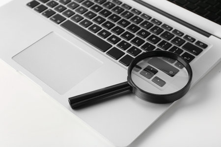 Modern laptop and magnifier on white table, closeup. internet search concept