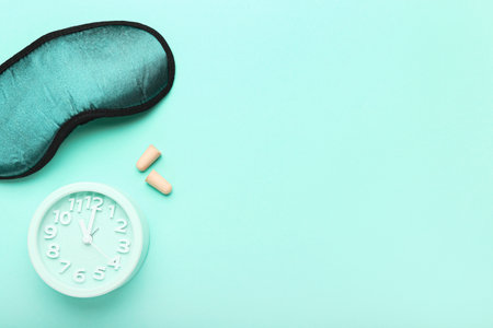 Earplugs, sleeping mask and alarm clock on color background