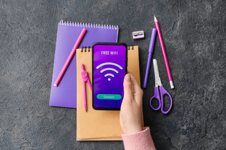 Woman holding mobile phone with WiFi symbol and different stationery supplies on dark background