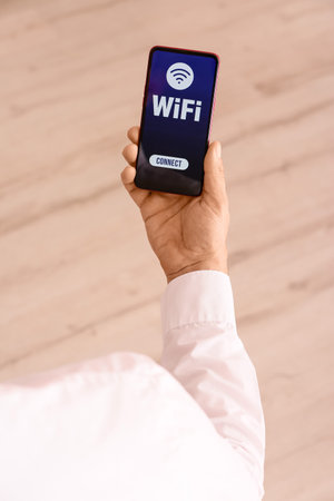 Male hand and mobile phone with WiFi symbol on light background, closeupの写真素材